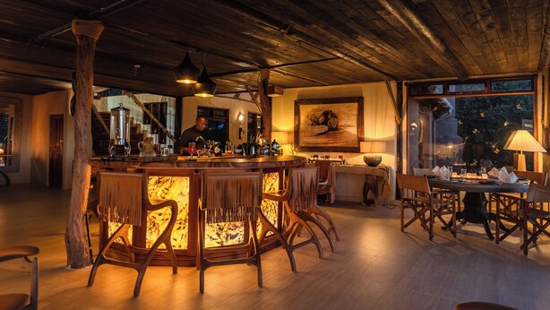 A bar area with wooden furniture and a large painting on the wall. - Cottar's Private Bush Villa (Ololaimutiek Village)