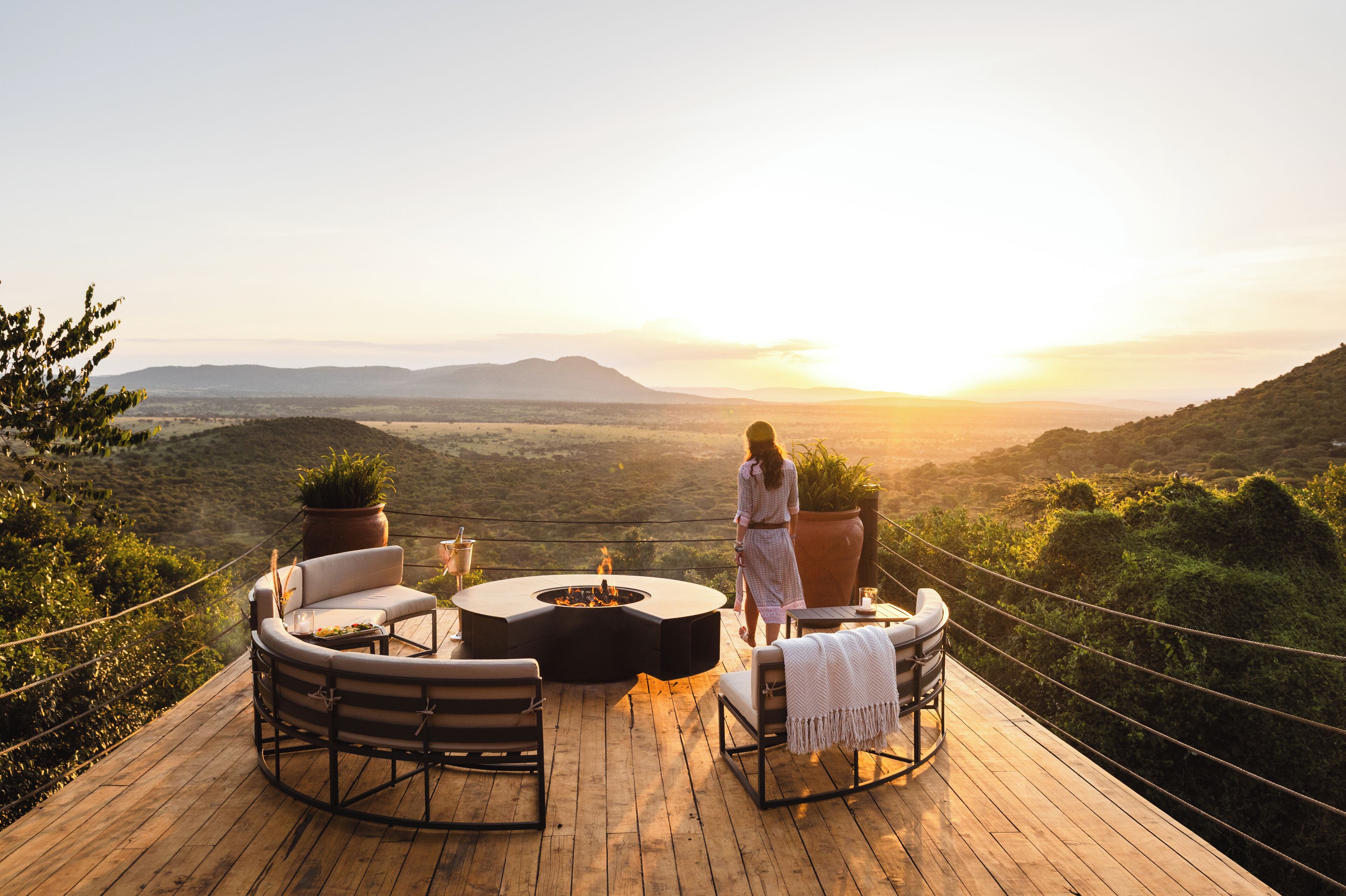 A wooden deck with outdoor furniture, a fire pit, and a view of a valley with mountains in the distance.