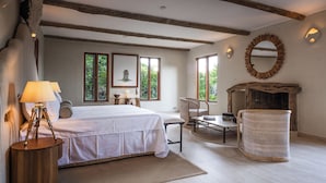 A bedroom with a bed, bedside table, lamp, chair, and a fireplace. - Cottar's Private Bush Villa (Ololaimutiek Village)