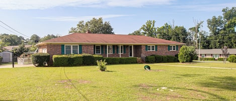 A single-story brick house with a red roof, a front porch, and a well-maintained lawn.