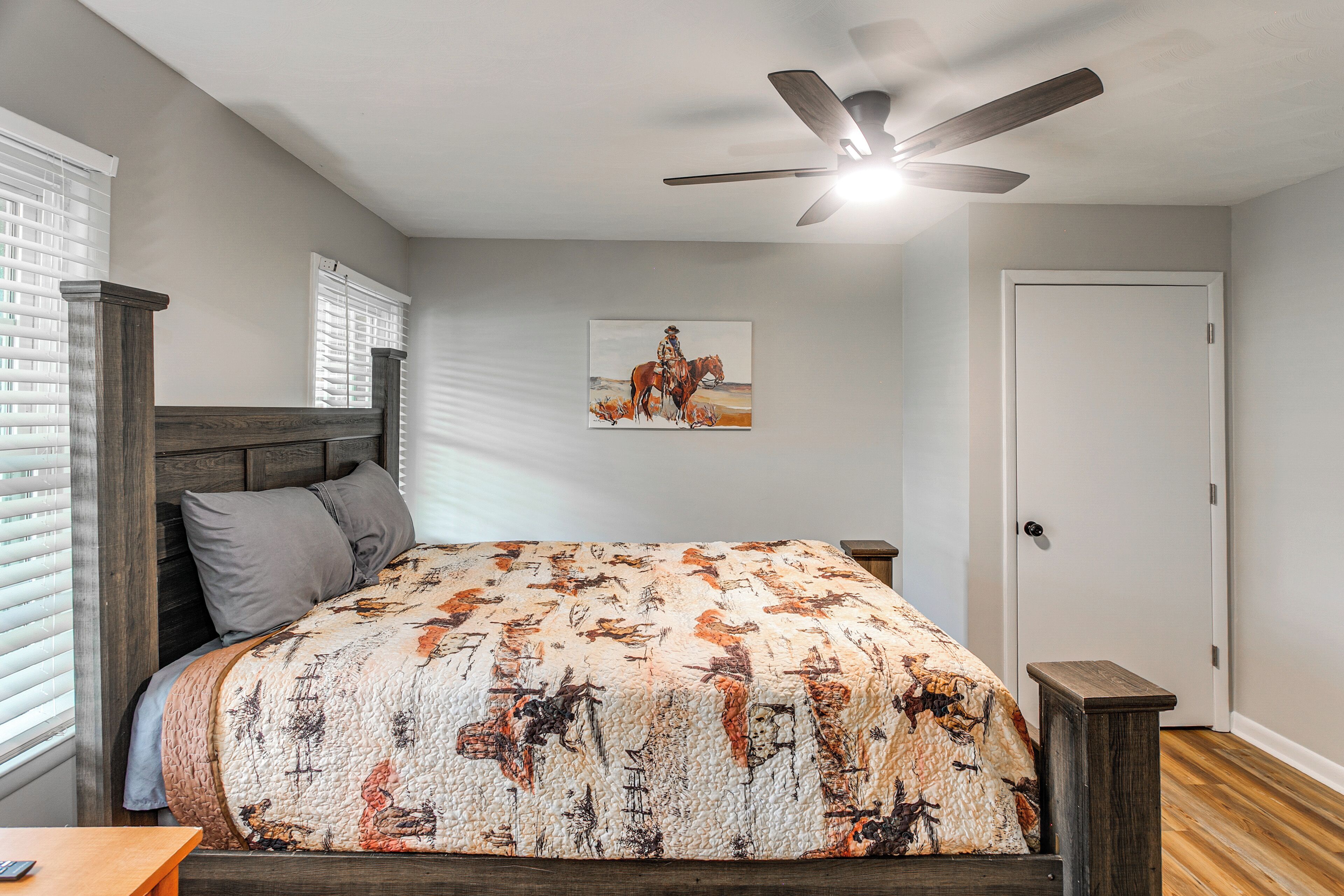 Een slaapkamer met een bed, plafondventilator, schilderij en een deur.