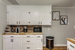 A kitchen with white cabinets, a coffee maker, a microwave, and a trash can.