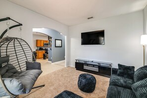 A modern living room with a hanging chair, a sofa, a TV, and a kitchen in the background. - Swim, Golf & Park-Hop! Family Home in Davenport (Davenport)