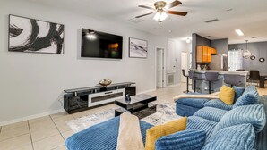 A modern living room with a flat-screen TV, a ceiling fan, and a bar area with stools. - Swim, Golf & Park-Hop! Family Home in Davenport (Davenport)