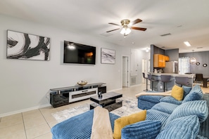A modern living room with a flat-screen TV, a ceiling fan, and a bar area with stools. - Swim, Golf & Park-Hop! Family Home in Davenport (Davenport)