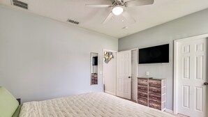 A bedroom with a bed, a ceiling fan, a TV mounted on the wall, and a dresser with drawers. - Swim, Golf & Park-Hop! Family Home in Davenport (Davenport)