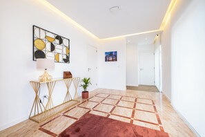 Ein moderner Flur mit einem geometrischen Fußbodenmuster, einer Zimmerpflanze, einem Beistelltisch mit Lampe sowie Bildern an den Wänden.