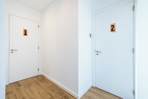 Twee witte deuren met houten nummerplaatjes, waarvan één het cijfer 1 en de andere het cijfer 2 heeft, in een hal met houten vloer.