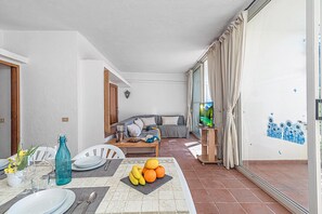 A living room with a sofa, a television, and a dining area with a table set for two. - Il Faro di Capo Ceraso (Olbia)