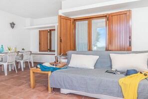 A living room with a sofa, a dining table with chairs, and wooden shutters on the windows. - Il Faro di Capo Ceraso (Olbia)