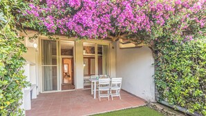 Eine Terrasse mit Tisch und Stühlen, umgeben von einem Garten mit rosa Blumen und einer Steinmauer.