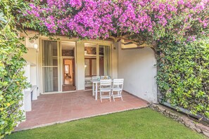 Eine Terrasse mit Tisch und Stühlen, umgeben von einem Garten mit rosa Blumen und einer Steinmauer.