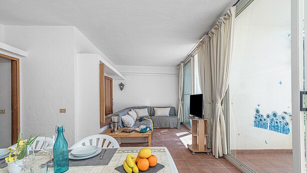Ein Wohnzimmer mit Sofa, Fernseher und Essbereich mit Tisch für zwei Personen.
