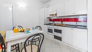 Eine Küche mit weißen Schränken, einer roten Spritzschutzleiste, einem Esstisch mit Stühlen und einer Kaffeemaschine.