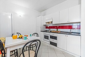 Eine Küche mit weißen Schränken, einer roten Spritzschutzleiste, einem Esstisch mit Stühlen und einer Kaffeemaschine.