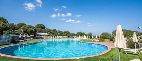 Una piscina con borde rojo, rodeada de césped artificial verde y protegida por sombrillas.
