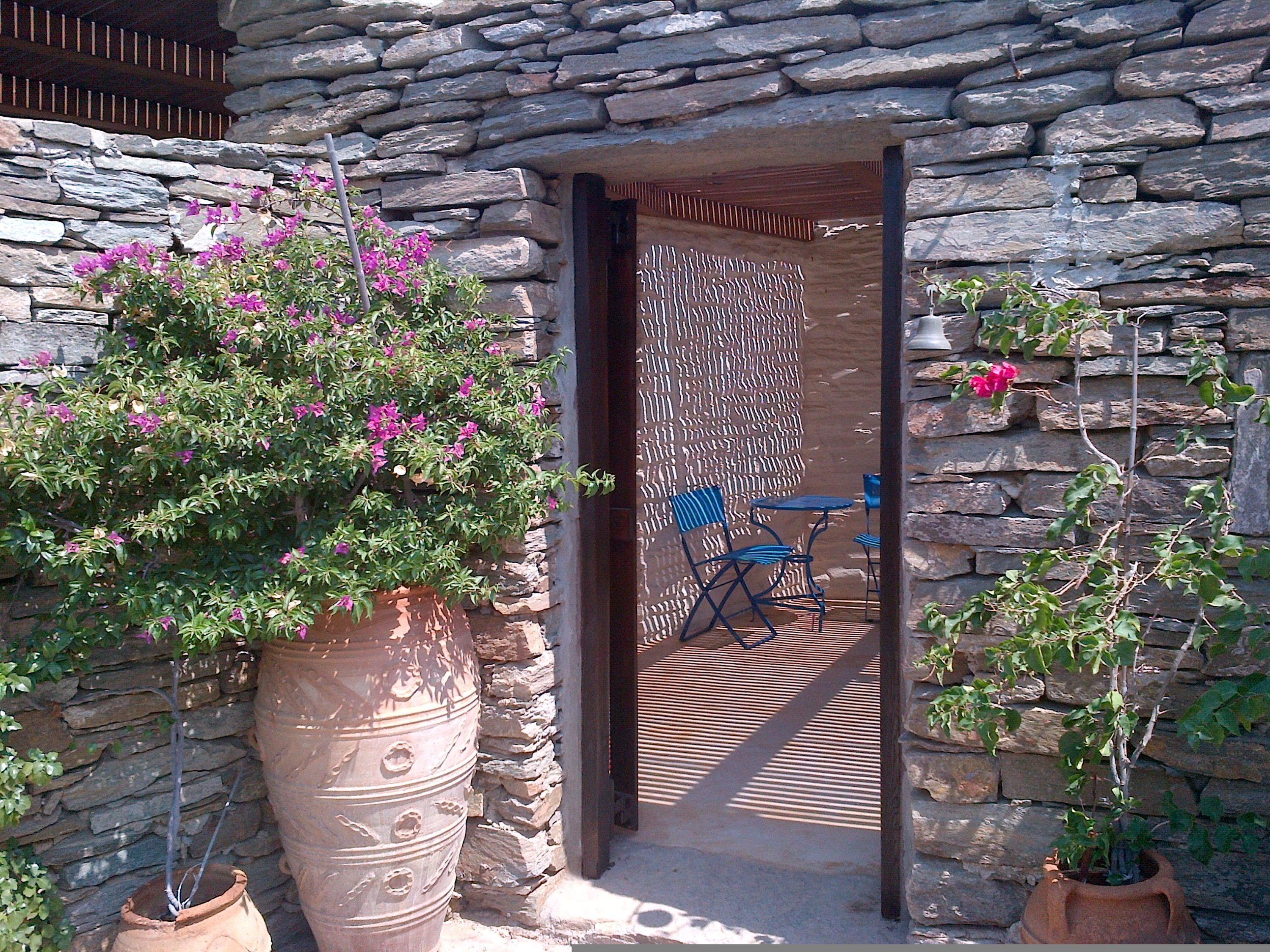 A stone wall entrance with a potted plant, a blue folding chair, and a wooden deck.