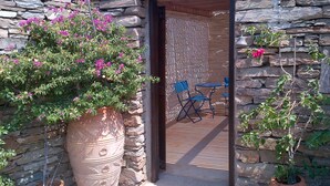 A stone wall entrance with a potted plant, a blue folding chair, and a wooden deck. - Zephyros Pool Tennis (Kea)