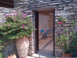 A stone wall entrance with a potted plant, a blue folding chair, and a wooden deck. - Zephyros Pool Tennis (Kea)