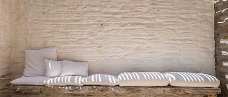 A stone bench with cushions against a textured wall.