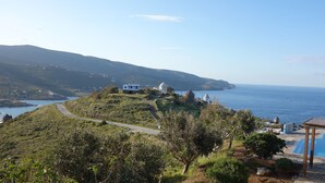 A coastal view with a road leading to a white building, a pool area, and a view of the sea. - Zephyros Pool Tennis (Kea)