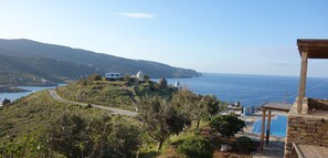 A coastal view with a road leading to a white building, a pool area, and a view of the sea. - Zephyros Pool Tennis (Kea)