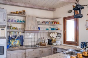 A kitchen with a tiled backsplash, wooden cabinets, and various kitchen appliances. - Zephyros Pool Tennis (Kea)