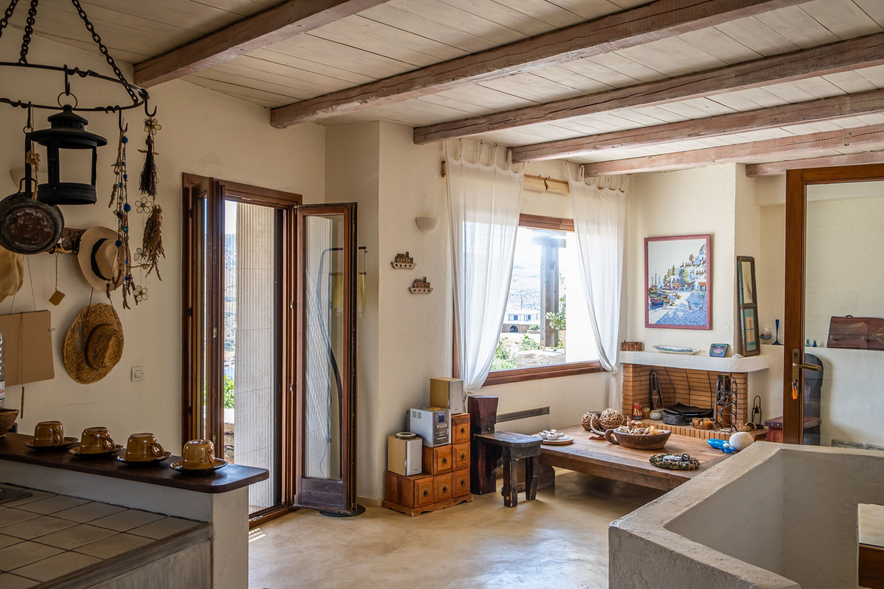 A rustic kitchen with wooden beams, a large window, and various kitchen items.