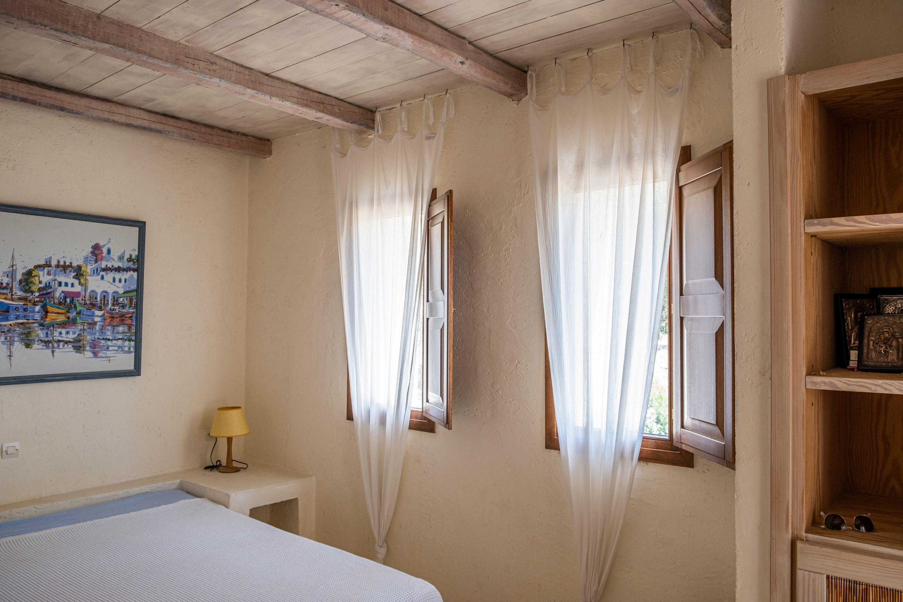 Une chambre à coucher avec un lit, une lampe de chevet, un tableau et une fenêtre avec des rideaux.