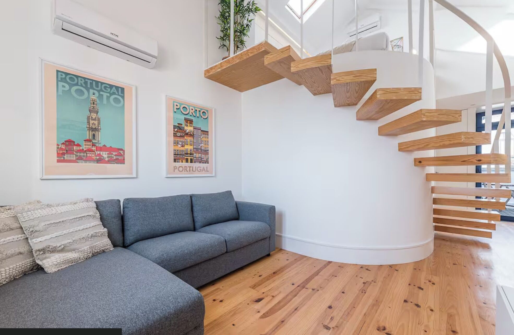 Un soggiorno moderno con un divano grigio, una scala in legno e due poster incorniciati del Portogallo.