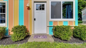 Una casa colorida con una puerta blanca, una ventana con cortina y un felpudo.