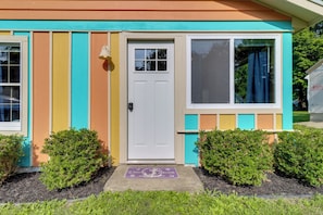 Uma casa colorida com uma porta branca, uma janela com cortina e um tapete de boas-vindas.