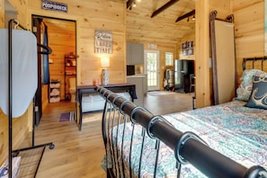 Interior de uma cabana de madeira com uma cama, uma escrivaninha, uma cadeira, uma TV e um letreiro que diz 'Relaxe, você está no tempo do lago'.