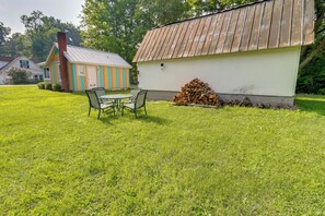 A grassy outdoor area with a small table and chairs, a stack of firewood, and a colorful shed.