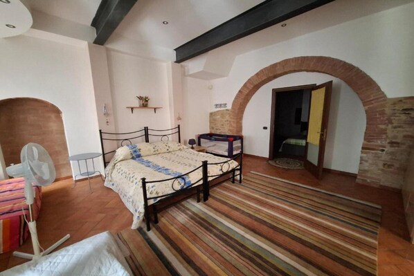 A bedroom with a bed, a fan, a small table, and an arched doorway. - Cozy Apartment in a Traditional Tuscan Stone Farmhouse (Rapolano Terme)