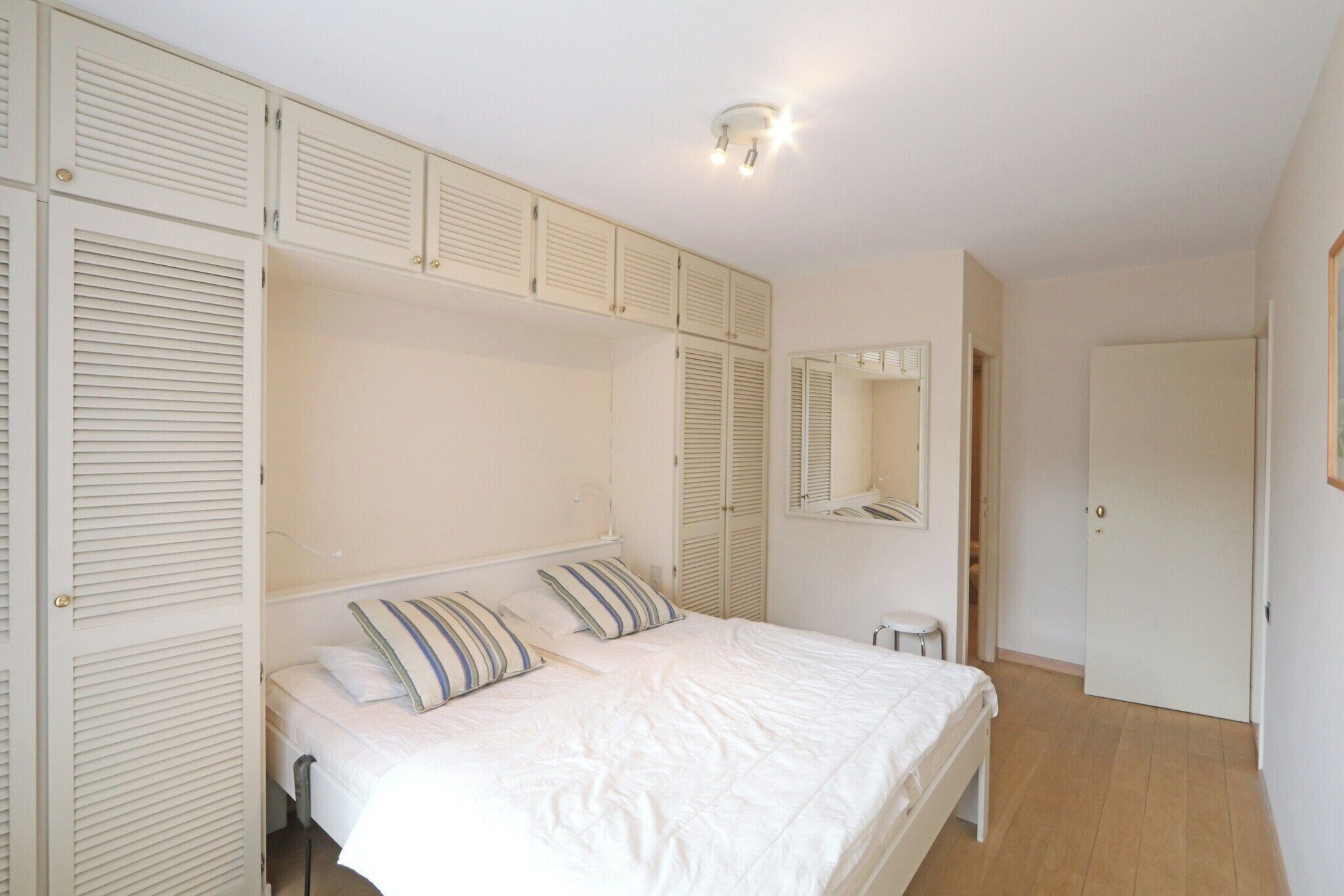 Ein Schlafzimmer mit einem Bett, einem Nachttisch, einem Spiegel und einem Schrank mit Klappläden.
