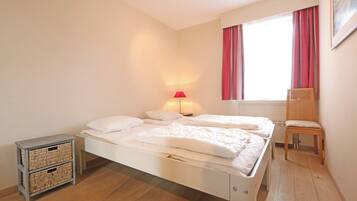A bedroom with two beds, a chair, a lamp, and a small storage unit.