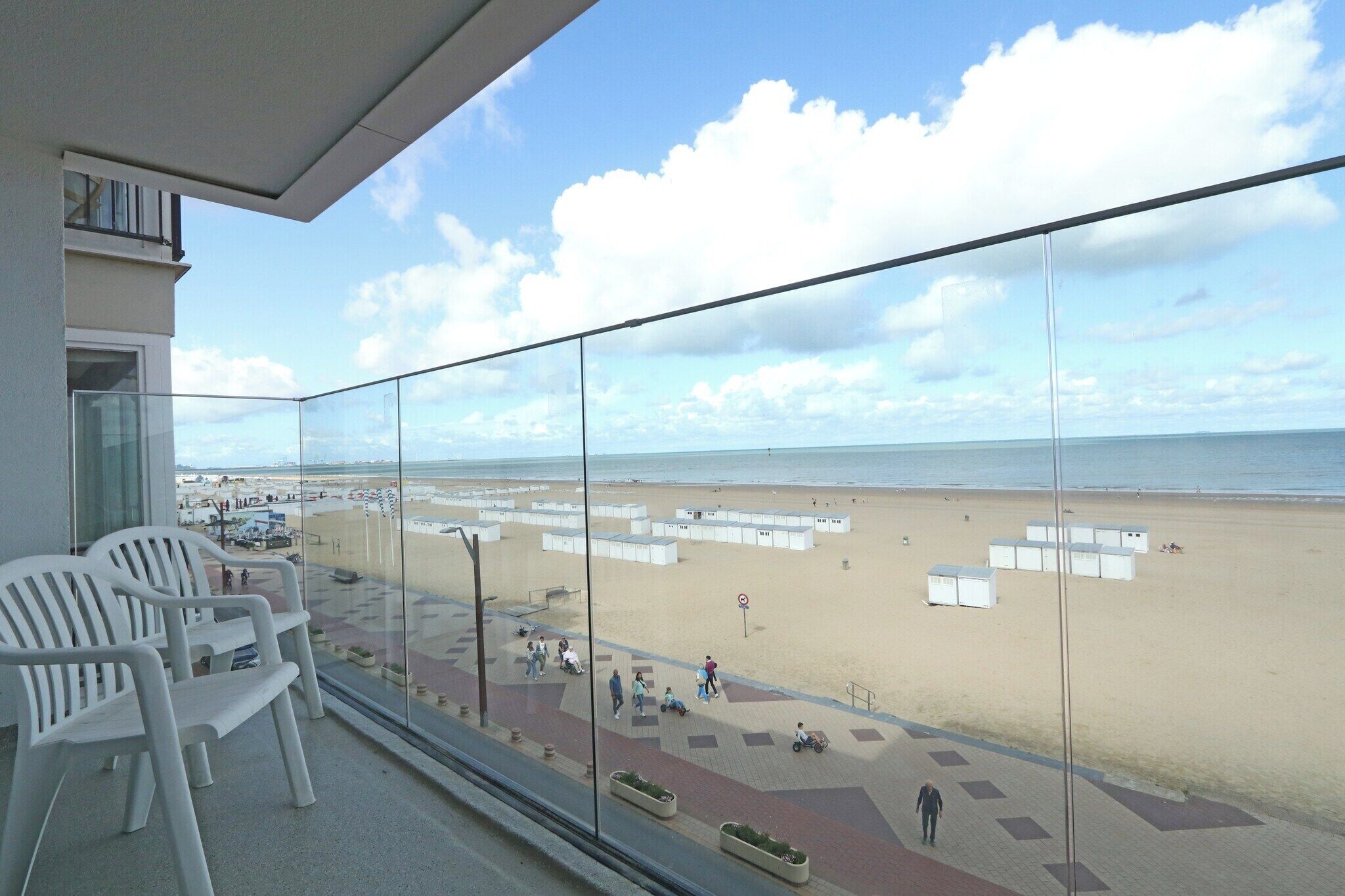Un balcon donnant sur une plage, des chaises en plastique blanches et un ciel dégagé.