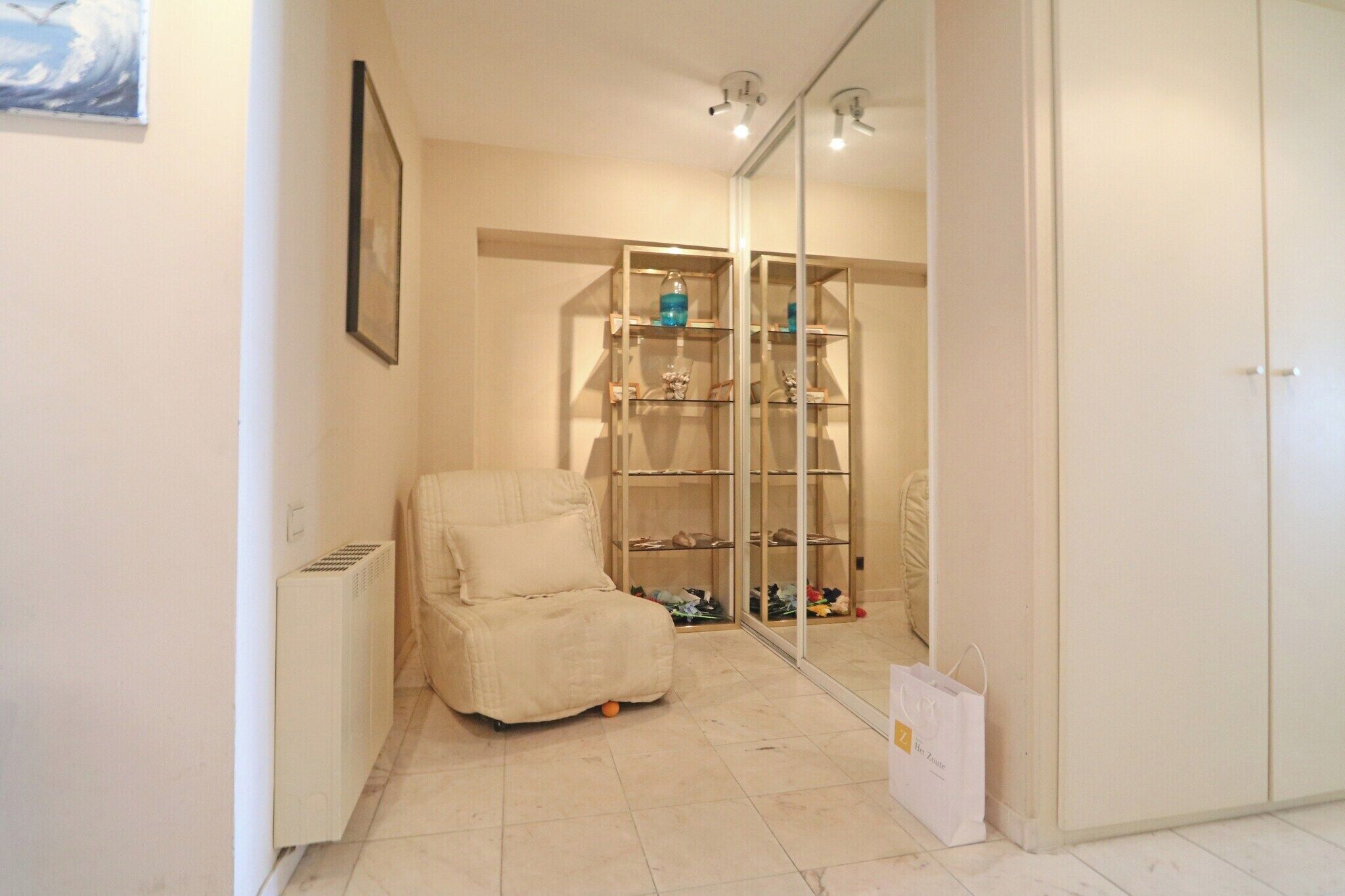 Een kamer met een witte fauteuil, een glazen vitrinekast met diverse spullen, en een witte radiator.