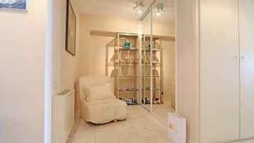Een kamer met een witte fauteuil, een glazen vitrinekast met diverse spullen, en een witte radiator.