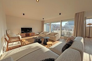 Een ruime woonkamer met een grote bank, een televisie en een balkon met uitzicht.