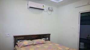 A bedroom with a bed, an air conditioner, a wall socket, and a door leading to a bathroom.