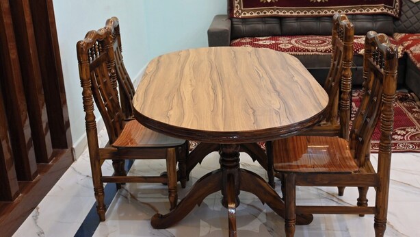 A dining table with four chairs, a sofa with a patterned throw, and a red and white floral blanket. - Sri Venkateswara Nilayam Home Stay (Tirupati)