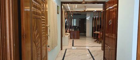 A hallway with a wooden door, a patterned curtain, a ceiling fan, and a view into a room with a dining table and chairs.