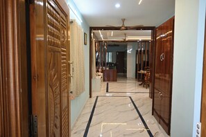 Un pasillo con puerta de madera, cortina estampada, ventilador de techo y vista a una habitación con mesa y sillas de comedor.