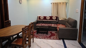 A room with a dining table, wooden chairs, a sofa, and a patterned rug. - Sri Venkateswara Nilayam Home Stay (Tirupati)
