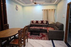 Una habitación con una mesa de comedor, sillas de madera, un sofá y una alfombra estampada.