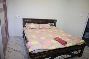 Una cama con una colcha estampada, cabecera de madera y una toalla enrollada sobre la misma.