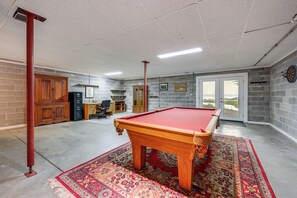 Uma mesa de bilhar numa sala com piso de concreto, tapete vermelho e parede de tijolos.