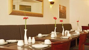 A dining area with tables set for service, a brown sofa, a large mirror, and wall-mounted light fixtures. - Sunday Hotel Stade Widukind Single Room (Stade)